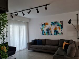סלון קטן ומעוצב עם ספה פינתית וקיר לבן המדגיש יצירת אמנות גדולה.